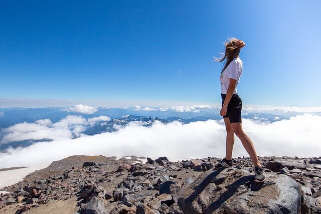 山の頂上に立つ女性が空と雲を背景に風を受ける様子